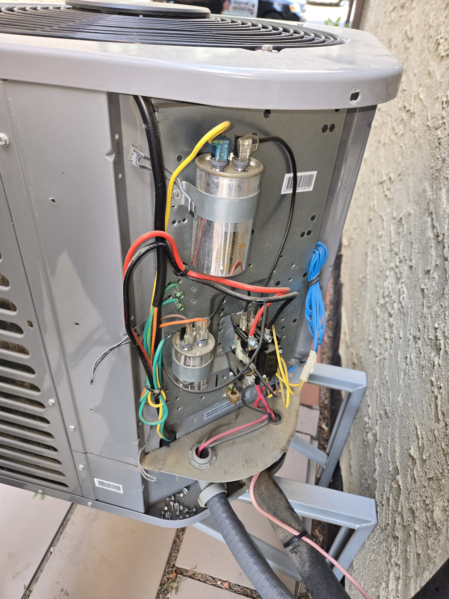 Technician replacing a run capacitor on an outdoor A/C condenser, service truck in background