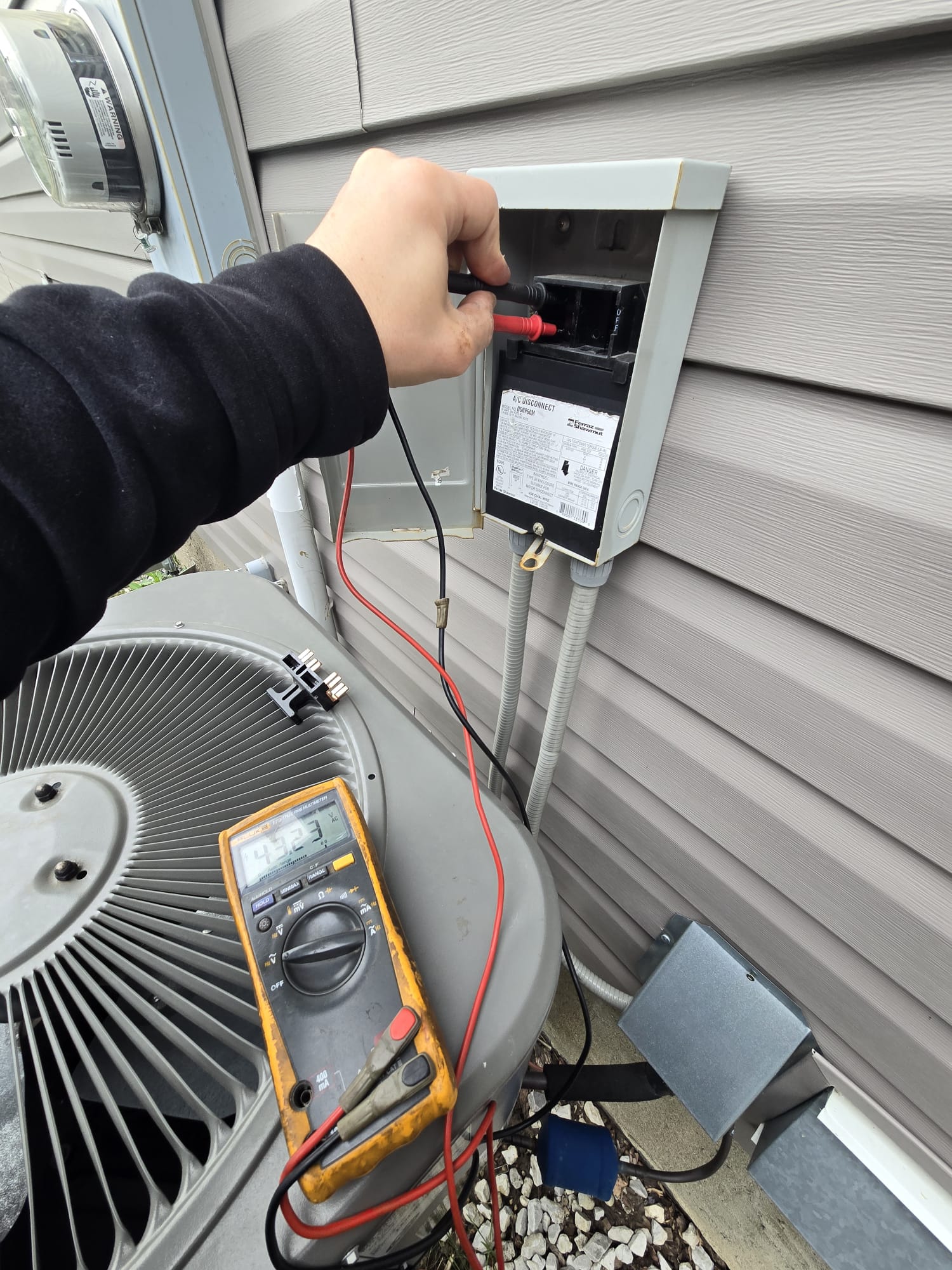 Technician testing voltage at an A/C disconnect box with a multimeter
